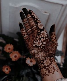 a woman's hand with henna on it and flowers in the back ground