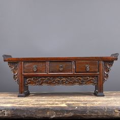 an old wooden table with drawers and carvings on the top, against a gray background