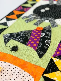 a close up of a patchwork quilt with a black spider on it's neck