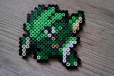 a green and black beaded brooch sitting on top of a wooden table