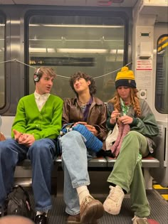 three people sitting on a subway car with hats and scarves hanging from their heads