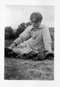 an old black and white photo of a young boy sitting on the ground with his dog