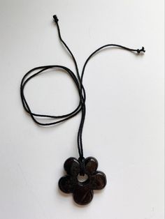 a black necklace with a flower shaped pendant hanging from it's side on a string