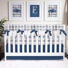 a baby crib with blue and white plaid bedding, framed pictures on the wall