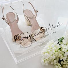 a pair of white shoes sitting on top of a clear box next to flowers and a bouquet