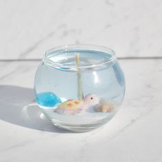 a fish bowl filled with water on top of a white countertop next to a candle