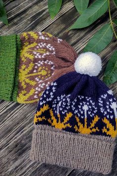 two knitted hats sitting on top of a wooden table next to green leafy branches