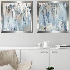 two paintings hanging on the wall above a white cabinet in a living room with a chair and coffee table