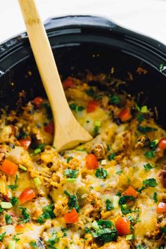 a wooden spoon in a black crock pot filled with meat and veggies