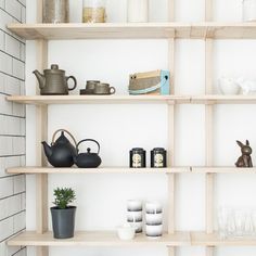 the shelves are filled with tea pots, cups and vases on them in front of a white brick wall