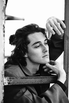 black and white photograph of a young man leaning against a rail with his hand on his chin