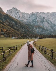 a woman walking down a road in the mountains with her back turned to the camera