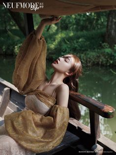 a woman sitting on top of a wooden bench next to a body of water with trees in the background