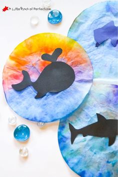 three paper plates with whale silhouettes on them and bubbles around the edges to make it look like they are floating