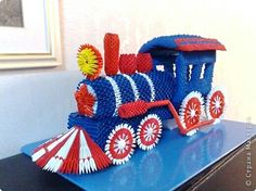 a blue toy train sitting on top of a table next to a window with red, white and yellow decorations