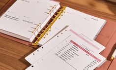 two open notebooks sitting next to each other on a wooden table with a pen