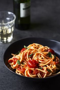 a plate of spaghetti with tomatoes and basil next to a bottle of wine on a table