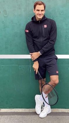 a man standing next to a green wall holding a tennis racquet