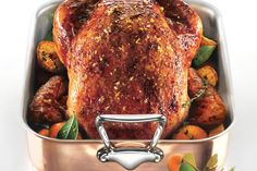 a roasted turkey in a roasting pan with oranges and herbs on the side