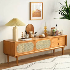 a living room with a wooden dresser and lamp on top of the sideboard next to a potted plant