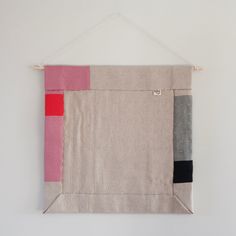 a piece of fabric hanging on a wall with some red and black squares in it