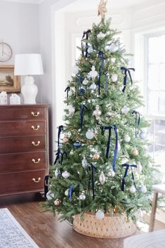 a decorated christmas tree with blue and white ornaments in a basket on the floor next to a window