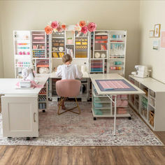 a woman sitting at a desk in front of a bookcase filled with craft supplies