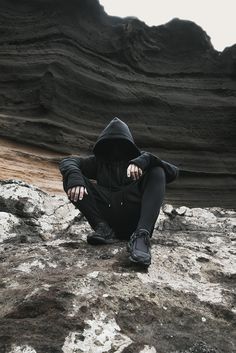 a person sitting on top of a rock covered in dirt and mud wearing a black hoodie