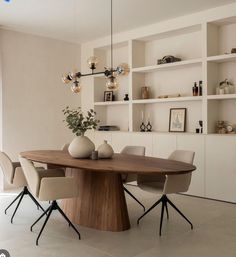 a dining room table with chairs and vases on it in front of bookshelves