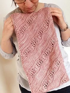 a woman holding up a pink knitted shawl in the shape of a flower