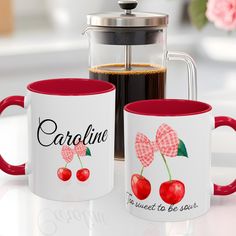 two red and white coffee mugs with cherries on them, next to a french press