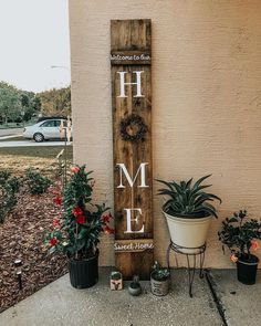 a wooden sign that says welcome to me and some potted plants next to it