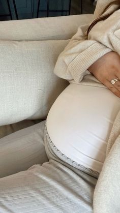 a pregnant woman sitting on a couch with her hands behind her back, holding the stomach