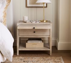 a nightstand with a lamp on top of it next to a bed