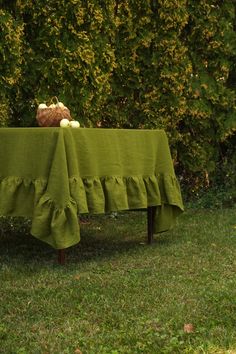 a green table cloth with ruffles on it sitting in the grass near some bushes