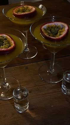 three desserts in glass dishes on a wooden table with two glasses and one is empty