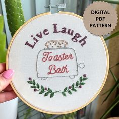 a hand holding up a embroidery hoop with the words live laugh toaster bar on it