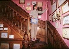 a woman standing on top of a stair case next to a wooden banister in a pink room