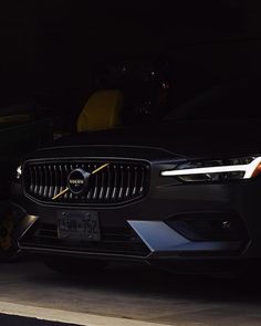 the front end of a black volvo car parked in a garage with it's lights on