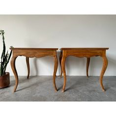 two wooden tables sitting next to each other near a potted plant on the floor