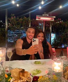 a man and woman taking a selfie at a dinner table with food on it