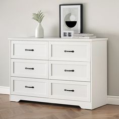 a white dresser with two vases on top of it next to a framed photograph