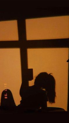 the silhouette of a person sitting in front of a window with a clock on it