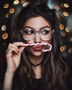 a woman wearing glasses and holding a candy cane in front of her face while looking at the camera