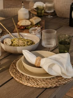 a wooden table topped with plates and bowls filled with food next to wineglasses