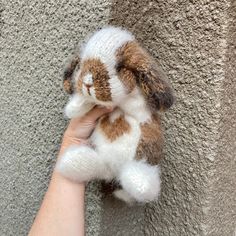 a hand holding a small stuffed animal on top of a cement wall next to a person's arm