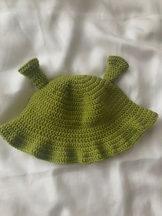 a green crocheted hat laying on top of a white bed sheet, with one ear flap open