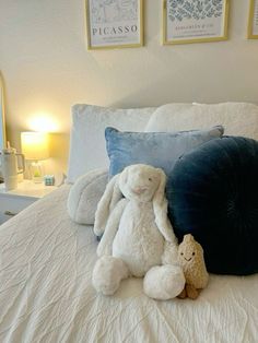 two stuffed animals sitting on top of a bed next to pillows and lamps in a bedroom