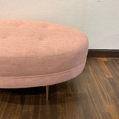 a pink ottoman sitting on top of a hard wood floor next to a white wall