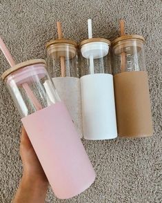 someone holding a pink cup with two straws in it next to three tumblers